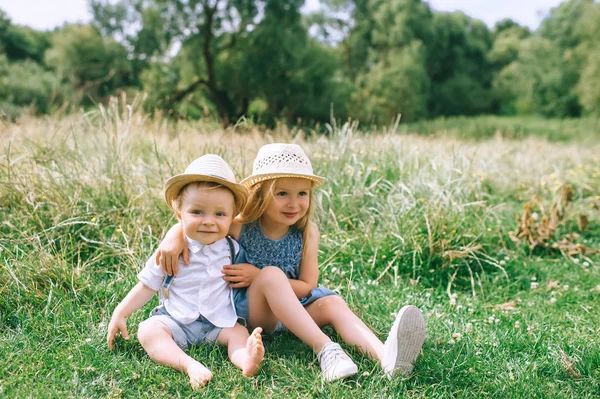 Adorable kids in straw hats sitting in field — Stock Photo