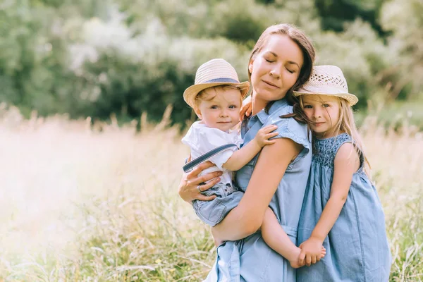 Schöne Mutter umarmt mit zwei Kindern auf dem Feld — Stockfoto