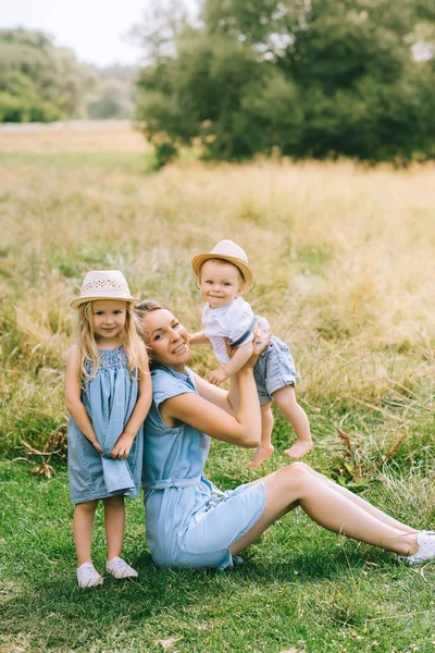 Приваблива мама з дітьми в солом'яних капелюхах у полі — стокове фото
