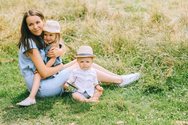 Hermosa madre feliz con dos niños sentados en el campo - foto de stock