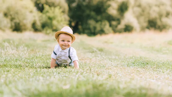 Niño con estilo en sombrero de paja arrastrándose en el campo - foto de stock