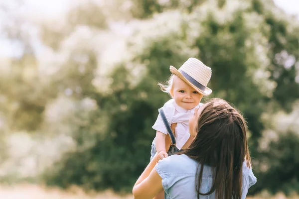 Stylish mother holding baby boy in straw hat — Stock Photo