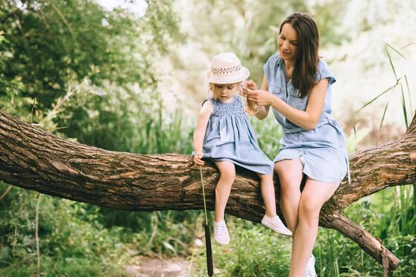 Mamá e hija sentadas en el árbol y pasando tiempo juntas en la naturaleza - foto de stock