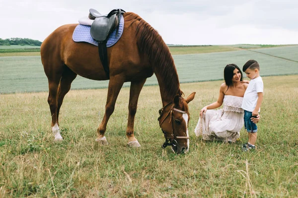 Mother and son squatting near horse on field — Stock Photo