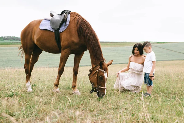 Madre e hijo mirando caballo marrón en el campo verde - foto de stock