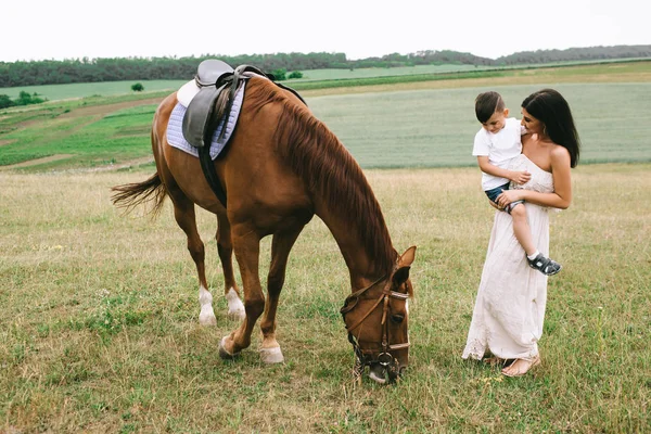 Мати тримає сина і дивиться на коня на полі — стокове фото