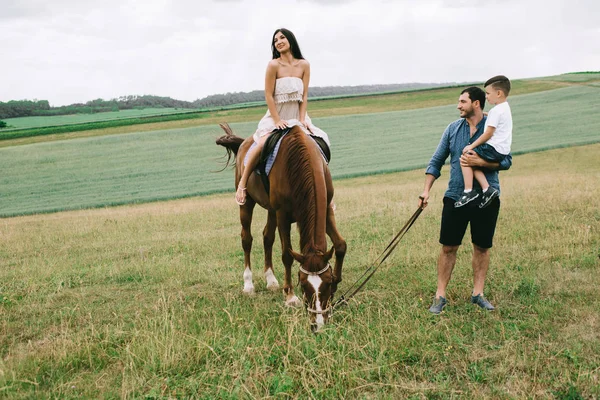 Padre e figlio guardando come madre a cavallo sul campo — Foto stock
