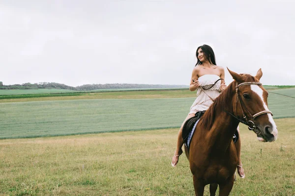Beautiful woman riding brown horse on field — Stock Photo
