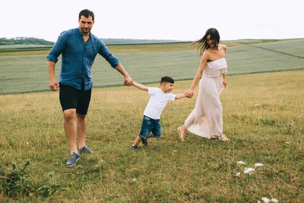 Padres e hijo tomados de la mano en el campo - foto de stock