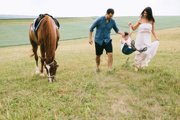 Familia cogida de la mano y caminando cerca de caballo en el campo - foto de stock
