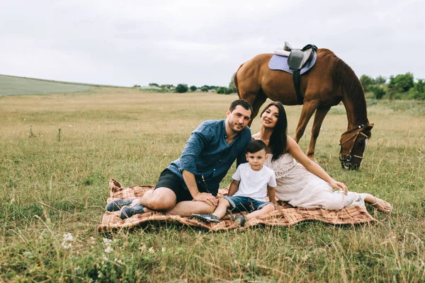 Eltern und Sohn sitzen auf einer Decke auf dem Feld und schauen in die Kamera — Stockfoto