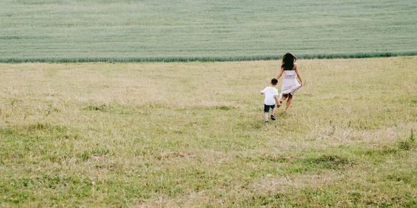 Visão traseira de mãe e filho correndo em campo — Fotografia de Stock