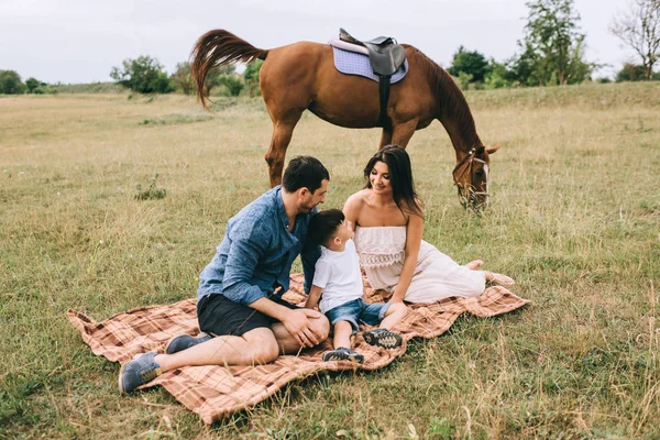 Батьки і син сидять на ковдрі на полі біля коня — стокове фото