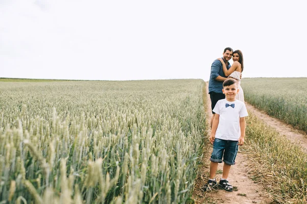 Батьки обіймають і щасливого сина, дивлячись на камеру на полі — стокове фото