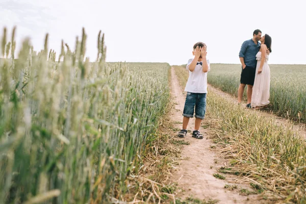 Parents kissing and son covering eyes on path in field — Stock Photo