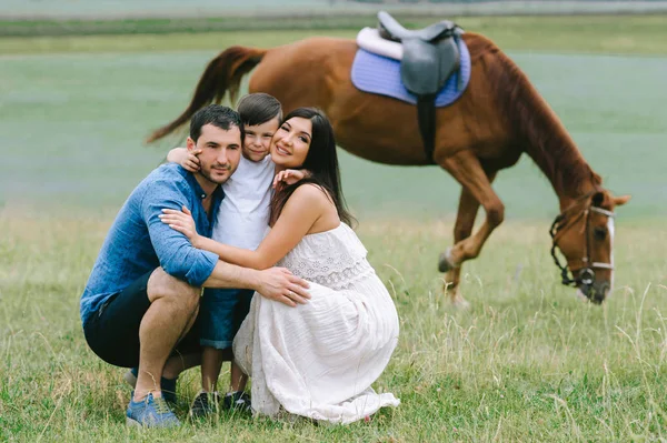 Parents and son squatting and hugging near horse on field — Stock Photo