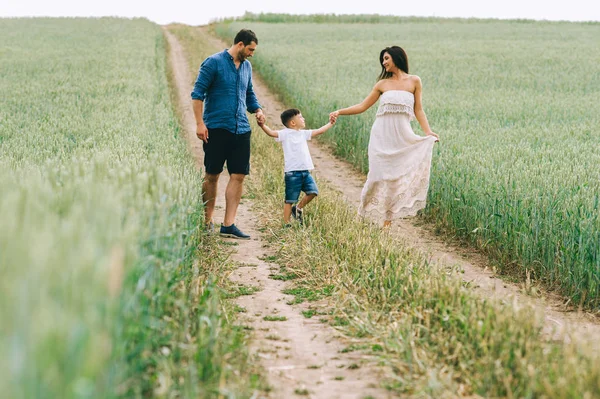 Padres e hijo tomados de la mano y caminando juntos en el camino en el campo - foto de stock