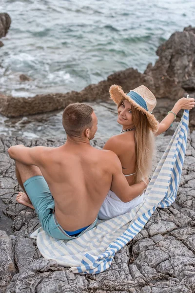 Vista de ángulo alto de hermosa pareja joven feliz sentados juntos en la playa rocosa en montenegro - foto de stock