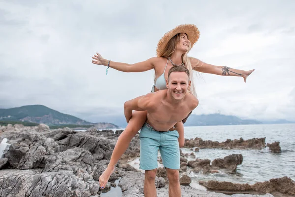 Feliz jovem casal piggybacking e se divertindo na praia rochosa em monten= — Fotografia de Stock