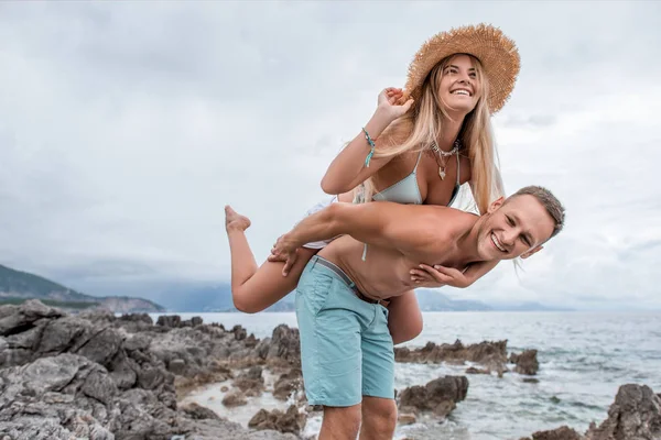 Low angle view of happy young couple piggybacking on rocky beach in montenegro — Stock Photo