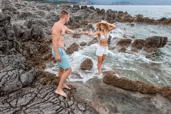 Happy young couple holding hands and smiling each other on rocky beach in montenegro — Stock Photo