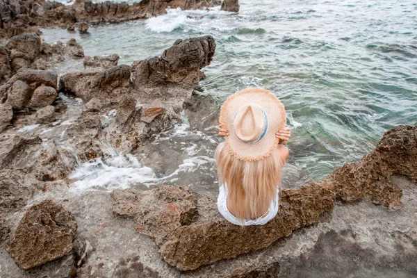 Высокий угол зрения молодой женщины в соломенной шляпе, сидящей на скальном пляже в Монтенегро — стоковое фото