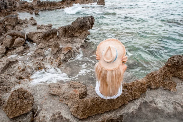 Vista de ángulo alto de la mujer joven en sombrero de paja sentado en la playa rocosa en montenegro — Stock Photo
