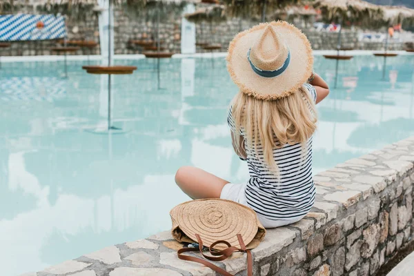 Вид сзади молодой женщины в соломенной шляпе, сидящей у бассейна в Монтенегро — стоковое фото