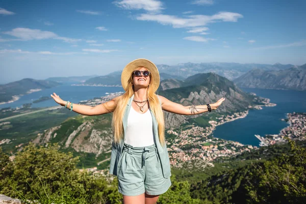 Mujer sonriente de pie con los brazos abiertos, la bahía de Kotor y la ciudad de Kotor en el fondo en Montenegro - foto de stock