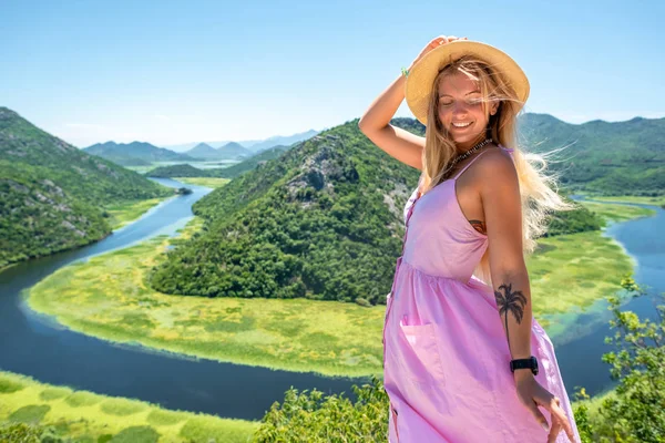 Femme souriante en robe rose et chapeau debout près de la rivière Crnojevica (Rijeka Crnojevica) au Monténégro — Photo de stock