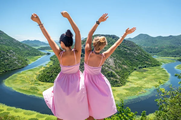 Vue de dos des femmes en robes roses debout avec les mains levées près de la rivière Crnojevica (Rijeka Crnojevica) au Monténégro — Photo de stock