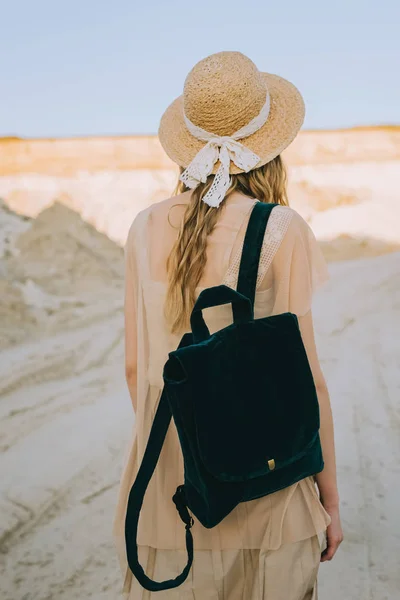 Вид ззаду дівчини в солом'яному капелюсі, що йде з рюкзаком в піщаному каньйоні — стокове фото