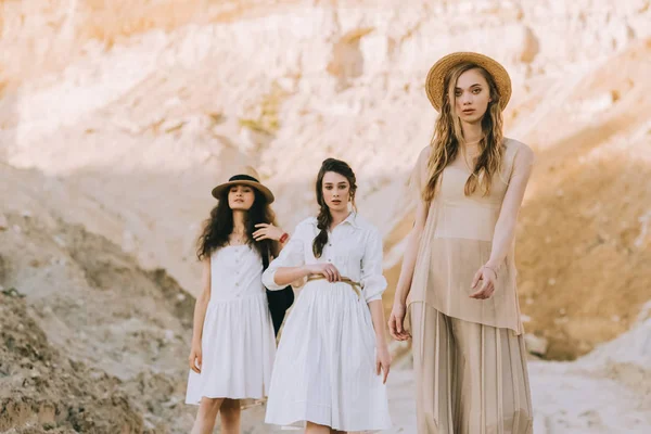 Beautiful young women in elegant dresses and straw hats posing in sandy canyon — Stock Photo