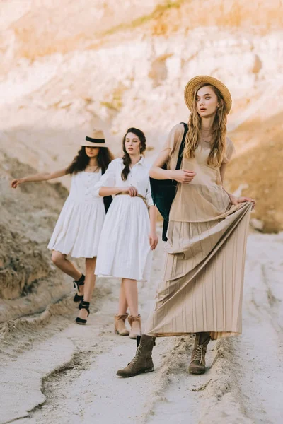 Elegant girls in stylish dresses and hats posing in sandy canyon — Stock Photo
