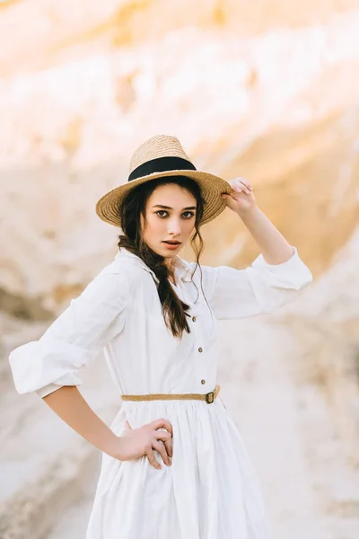 Привлекательная девушка позирует в элегантном платье и соломенной шляпе в песчаном каньоне — стоковое фото
