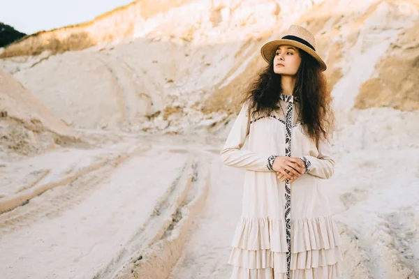 Beautiful curly girl posing in dress and straw hat in sandy canyon — Stock Photo