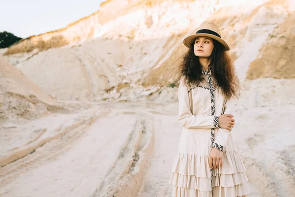 Привлекательная кудрявая девушка позирует в соломенной шляпе в песчаном каньоне — стоковое фото