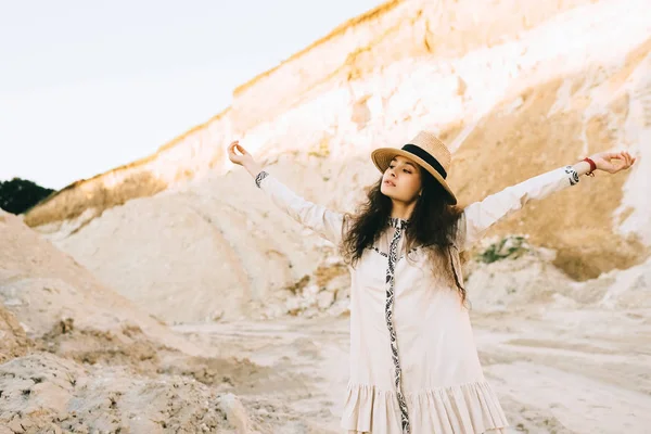 Beautiful curly girl in straw hat standing with outstretched hands in sandy canyon — Stock Photo