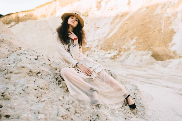 Элегантная девушка позирует в модном платье и соломенной шляпе в песчаном каньоне — стоковое фото