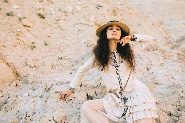 Stylish curly girl posing in straw hat in sandy canyon — Stock Photo