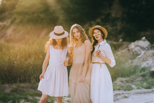 Beautiful girls in straw hats holding plastic cups with coffee latte — Stock Photo