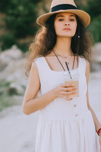 Atractiva chica elegante en sombrero de paja sosteniendo taza desechable con café con leche - foto de stock