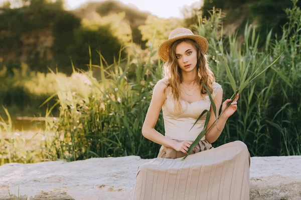 Elegante menina elegante em chapéu de palha sentado no chão perto da lagoa — Fotografia de Stock