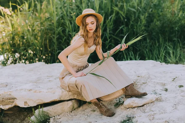 Attractive blonde girl in elegant dress and straw hat sitting on ground — Stock Photo