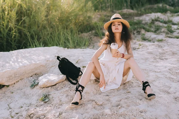 Jolie fille avec sac à dos et café latte dans une tasse jetable assis sur le sol — Photo de stock