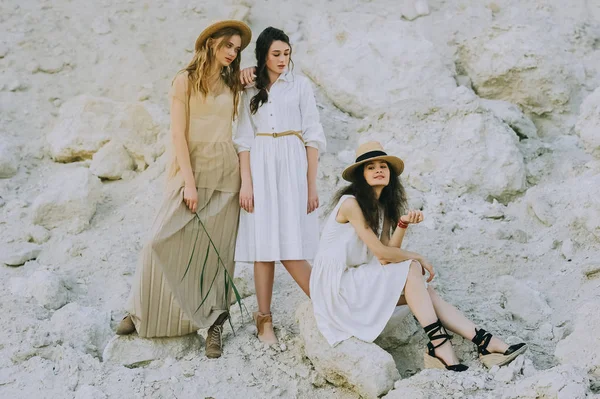 Beautiful friends in elegant dresses and straw hats posing together in sandy canyon — Stock Photo