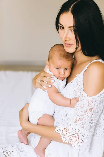 Gros plan de belle jeune mère avec son mignon bébé assis sur le lit à la maison — Photo de stock