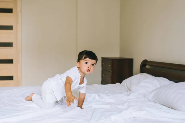 Entzückendes kleines Kind in weißer Kleidung, das auf dem Bett kriecht — Stockfoto