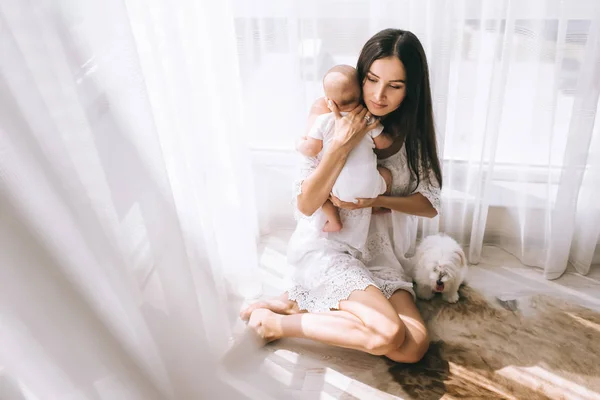 Belle jeune mère et bébé assis sur le sol à la maison avec chien bichon mignon — Photo de stock