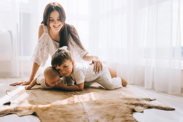Счастливая молодая мама проводит время с детьми, сидя на полу — стоковое фото